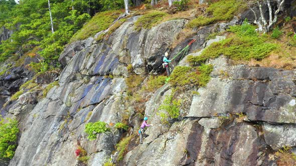 Aerial footage tilting up as young female climber approaches her instructor at top of cliff in Maine