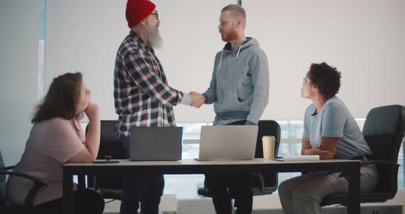 Hipster Senior Boss Shaking Hand of Young Male Employee at Team Meeting in Office