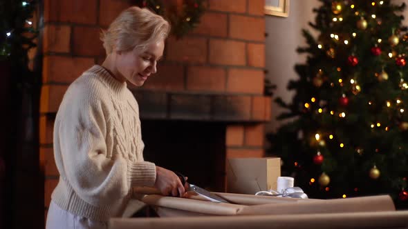 Happy Young Woman Cutting Wrapping Craft Paper with Scissors to Wrapping Gift Boxes of Christmas