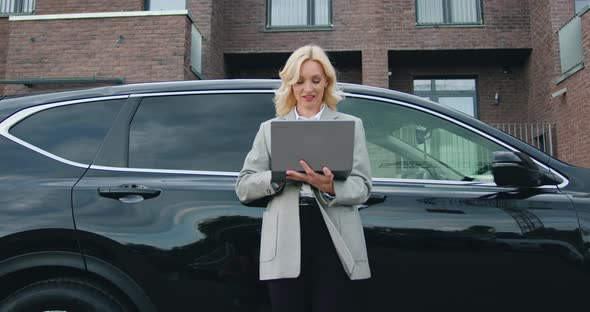 Business Woman in Jacket Using Laptop by the Car During Coffee Break, Outside.