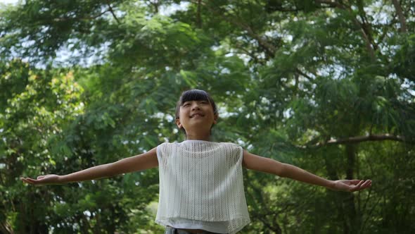Asian little girl playing outdoor in slow motion, Spinning and smiling and raising hands in the air