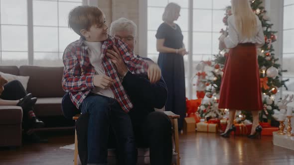 Boy Comes to Sit on a Chair with His Grandad to Talk at Christmas Celebration