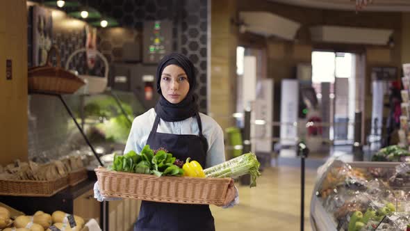Muslim Woman in Hijab Walks with Basket of Fresh Vegetables in the Supermarket