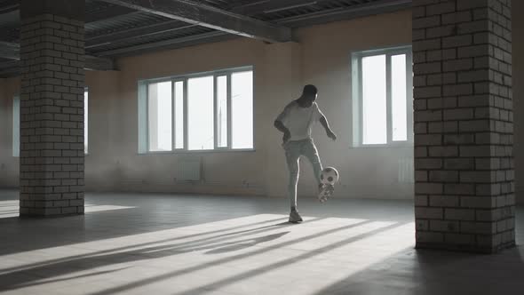 Black Man Football Soccer Player Practicing Tricks Kicks and Moves with Ball Inside Empty Covered