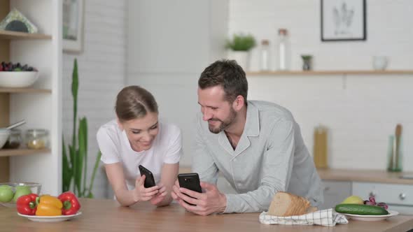 Happy Young Couple Using Smartphone in Kitchen