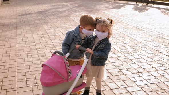 Two Children in Medical Masks Walk in Park with a Pram During the Coronavirus.