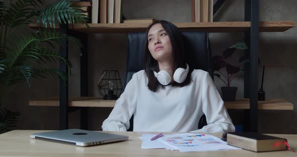 Asian Woman Leaning on the Back of an Armchair After a Hard Working Day and Looking Away