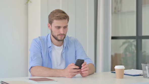 Attractive Young Creative Man Using Smartphone in Office