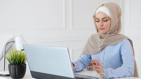 Young Muslim Woman Is Listening Music in Earphones Using Laptop and Enjoying It