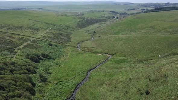 Panoramic aerial of a moorland valley with a river and forest in the foreground. Dartmoor, England