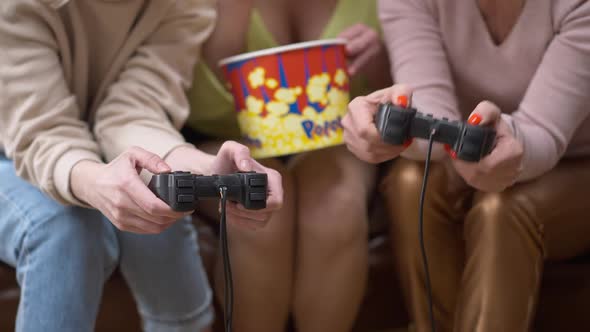 Unrecognizable Adult Women with Joysticks Playing Video Game As Friend Eating Popcorn Enjoying