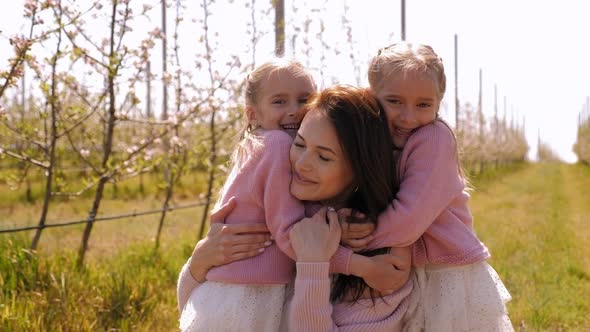 Portrait of a Young Mother with Twin Daughters in a Spring Apple Orchard.