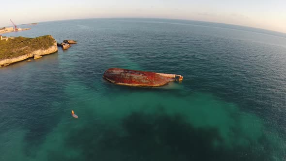 Aerial shot of young woman sup standup paddleboarding near a shipwreck in the Caribbean.