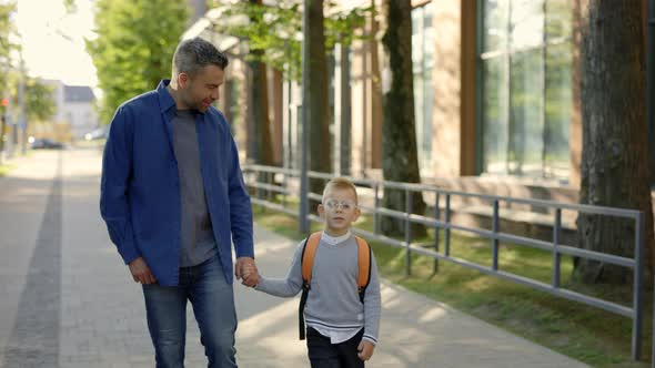 Close View of the Father Holds His Son's Hand They Leave School Together and Talk About How the Day