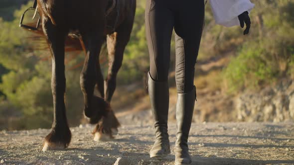 Front View Legs of Unrecognizable Horse and Woman Strolling in Slow Motion on Dusty Mountain Road