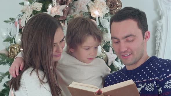 Young Father Reading Christmas Tale, While Mother and Their Happy Son Whispering Secretly