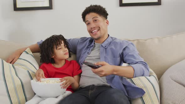 Happy biracial man and his son watching tv together