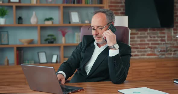 Bearded Businessman CEO Answering on Phone Call While Using Computer.