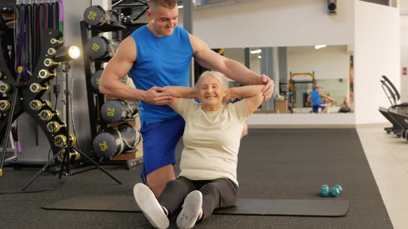 Young Handsome Coach Helps the Older Woman Perform Stretching