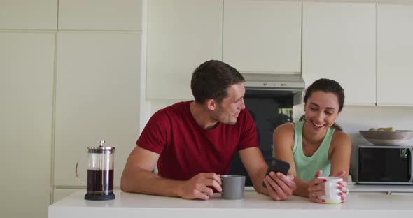 Happy caucasian couple drinking coffee and using smartphone