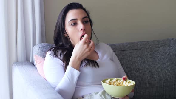 Beautiful woman eating popcorn on sofa 4k