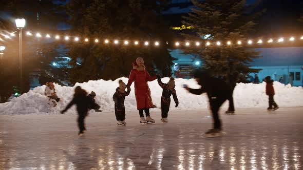 A Family of Young Mother and Two Kids Skating on the Decorated Ice Rink Holding Their Hands