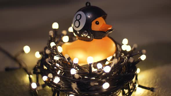 Closeup Shot of Rubber Duck in Hand Made Motorcycle Helmet on Background of Christmas Garland