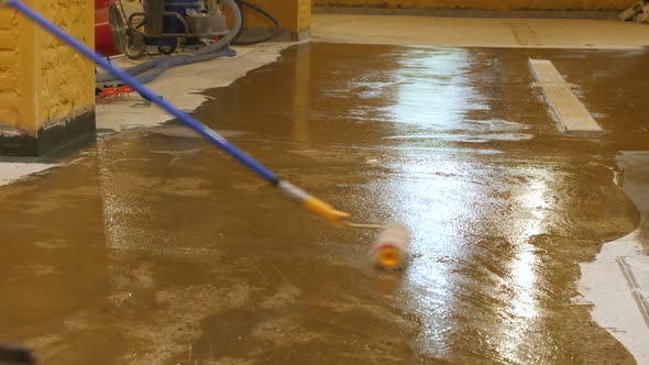 The Process of Applying a Primer with a Roller and a Spatula on a Concrete Floor