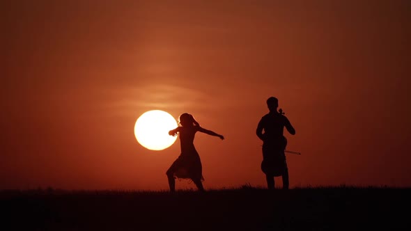 Silhouette of Woman Dancer and Cellist Opposite Huge Sun
