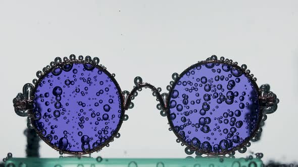 Round Stylish Sunglasses Covered with Air Bubbles in Transparent Water on a White Background