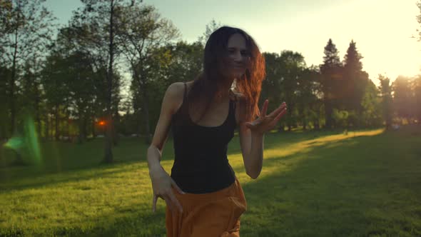 Young Woman Dancing on Grass in Park at Sunset.