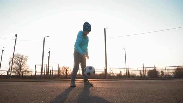 A Child Girl Playing with Soccer Ball Under Sun Light. Green Field in City Park at Sunny Day. Action