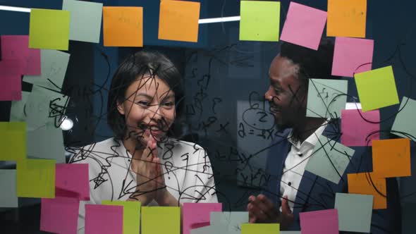 Happy AfricanAmerican Colleagues Look at Glassboard with Notes and Gesture Highfive