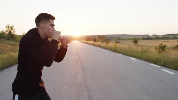 View of Young Kickboxer Training Kicks on Country Road Singly During Sunset