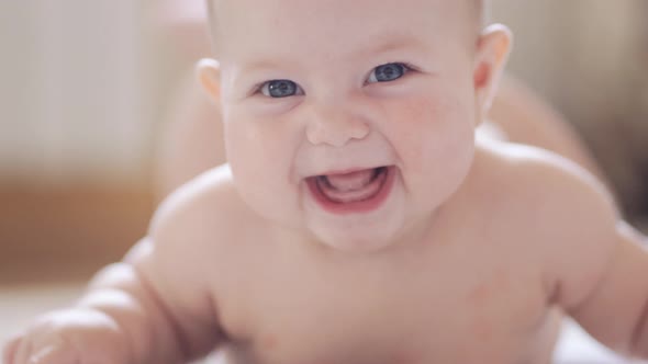 A little baby is lying on his belly against a light background and smiling