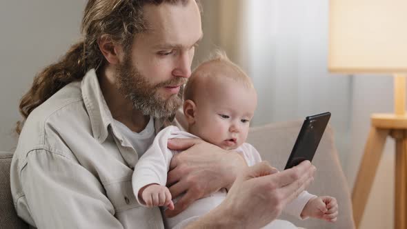 Adult Caucasian Father Bearded Daddy with Little Daughter Son Infant Newborn Sitting at Home Sofa