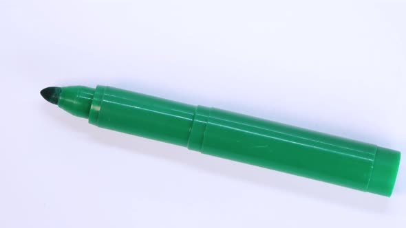 Green marker pen rotating on white surface background, macro shot close up view detail.