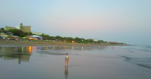 Aerial drone view of a young woman walking on the beach at sunset.