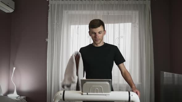 Male athlete is wiping face with towel during fitness cardio exercises on treadmill at home