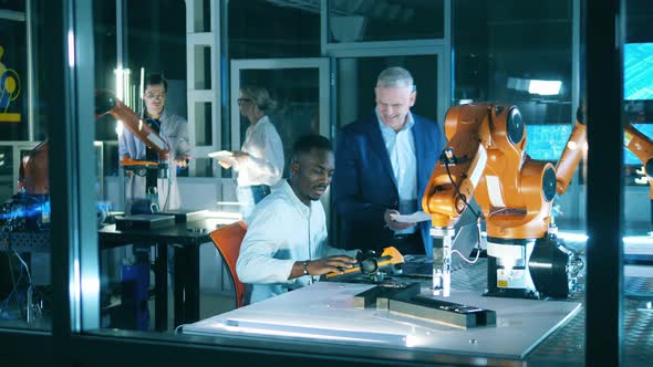 African Man Is Observing a Robotic Device with a Group of Engineers