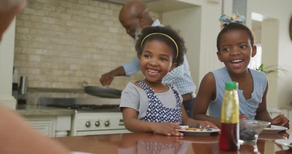 Happy african american grandparents with granddaughters having breakfast and talking