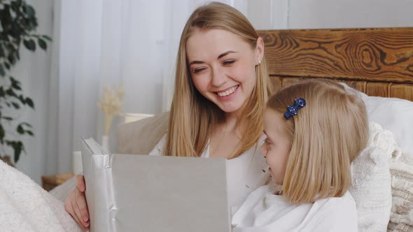 Portrait Mom and Daughter Lie in Bed Resting Hugging in Bedroom at Home Mother Reads Book at Night