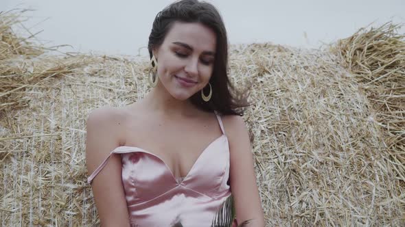 Portrait of Elegant Smiling Lady in Dress with Naked Legs Leaned on Haystack