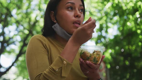 African american woman wearing face mask eating salad in sity park