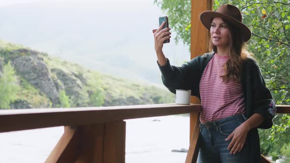 Attractive Brunette in a Hat and a White Shirt with Peas Talking on a Cell Phone, Taking a Selfie on