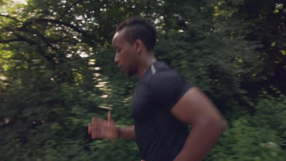 Side View of Muscular Afro Man Running in Green Forest