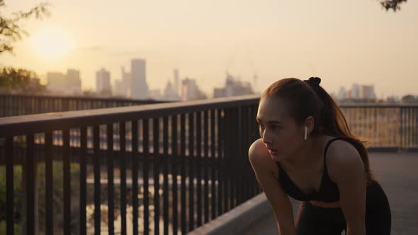 Young woman athlete running resting exhausted after a cardio workout in the urban city sunset. 