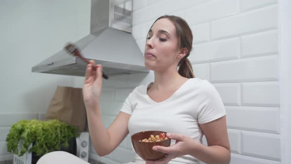 Joyful Woman Is Singing And Using Her Wooden Fork As Microphone While Eating Meal In The Kitchen