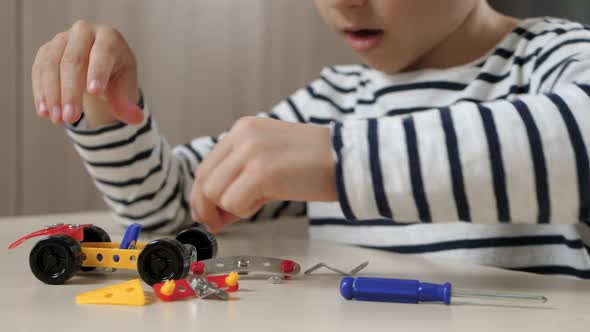 A Child Designs a Model of a Small Toy Car. A Happy Child Plays with a Constructor While Sitting at