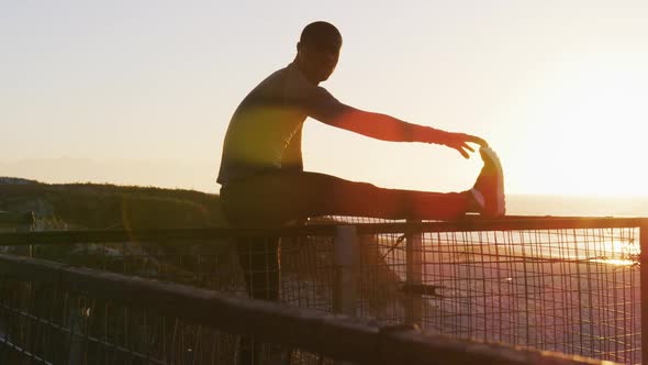 Focused african american man stretching, exercising outdoors by seaside at sunset